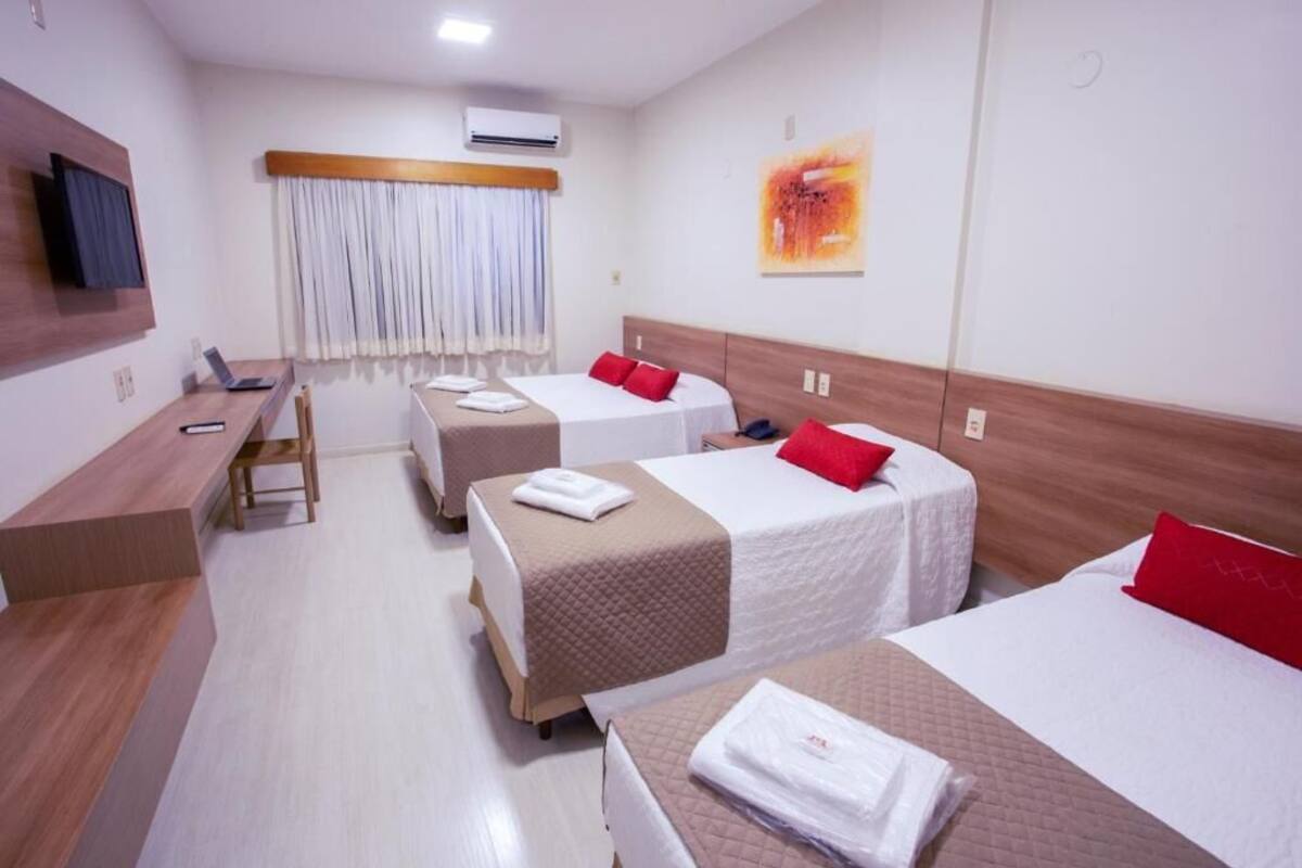 A hotel room with two beds, a desk, a chair, a TV, and a window with curtains.