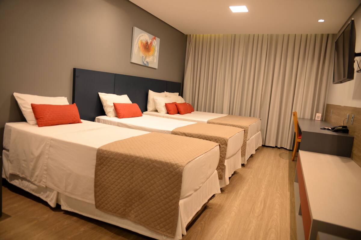 A hotel room with three beds, a desk, and a television.