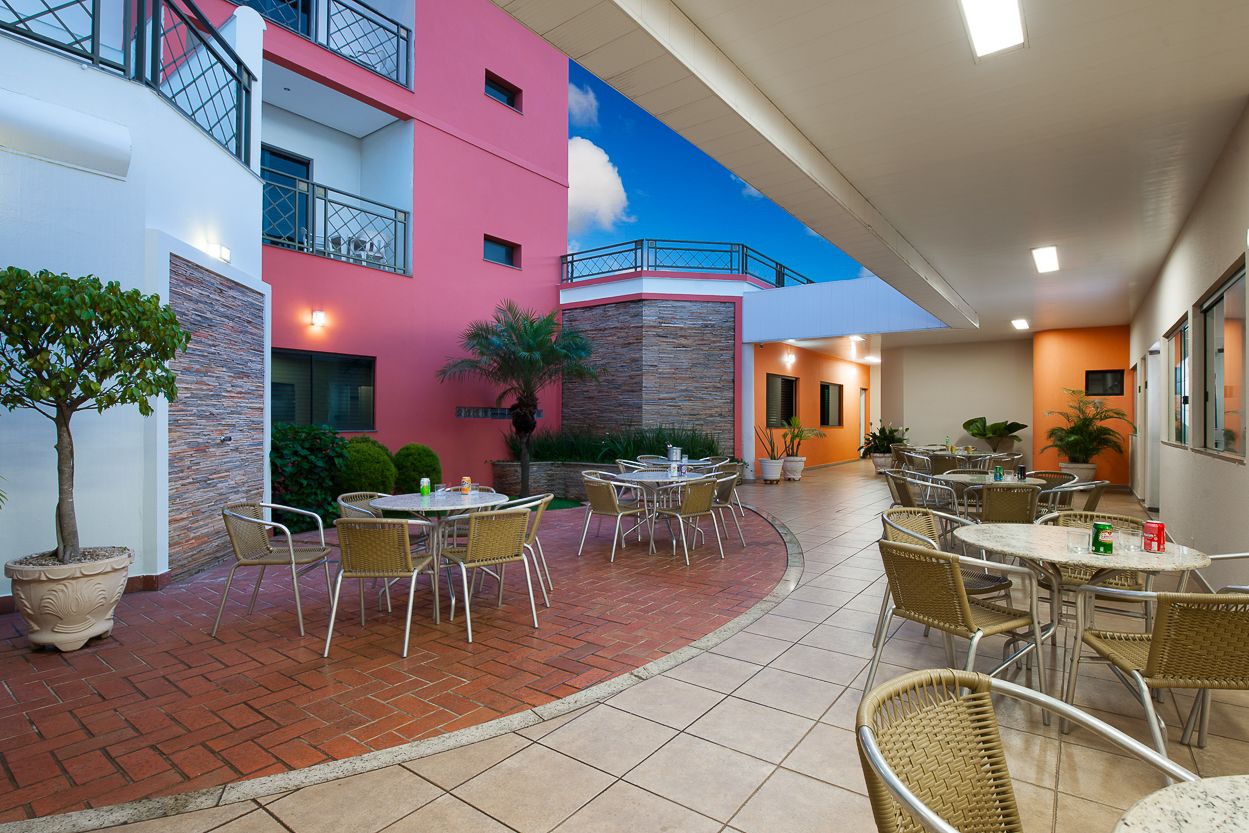 Un patio con mobiliario exterior, un edificio rosa y un cielo azul despejado.