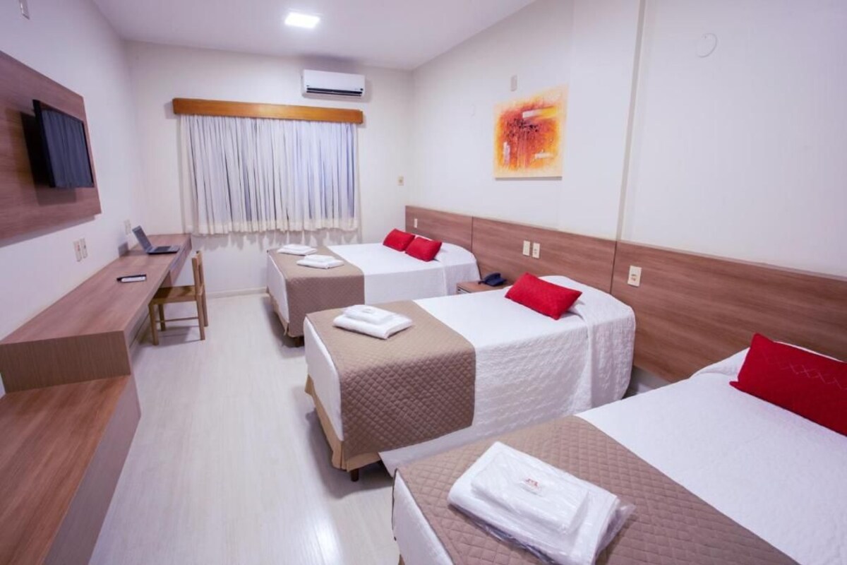 A hotel room with two beds, a desk, a chair, a TV, and a window with curtains.
