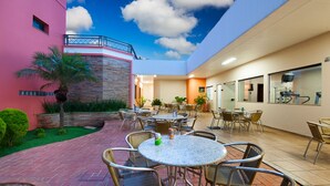 An outdoor patio area with round tables and chairs, a stone wall, and a pink building. - Carlton Plaza Hotel Uberlândia (Uberlandia)