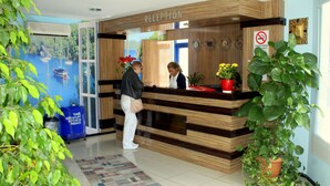 A reception area with a wooden reception desk, a large window with a view of boats, and potted plants.