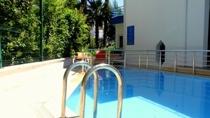 A swimming pool with metal ladders, surrounded by a fence and greenery.