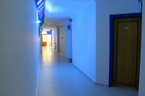 Un pasillo con una puerta de madera a la derecha, un muro azul y blanco a rayas a la izquierda y un piso de baldosas.