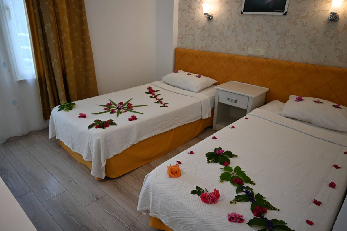 Habitación de hotel con dos camas, cada una con cubrecama y almohadas blancas, y una mesita de noche pequeña.