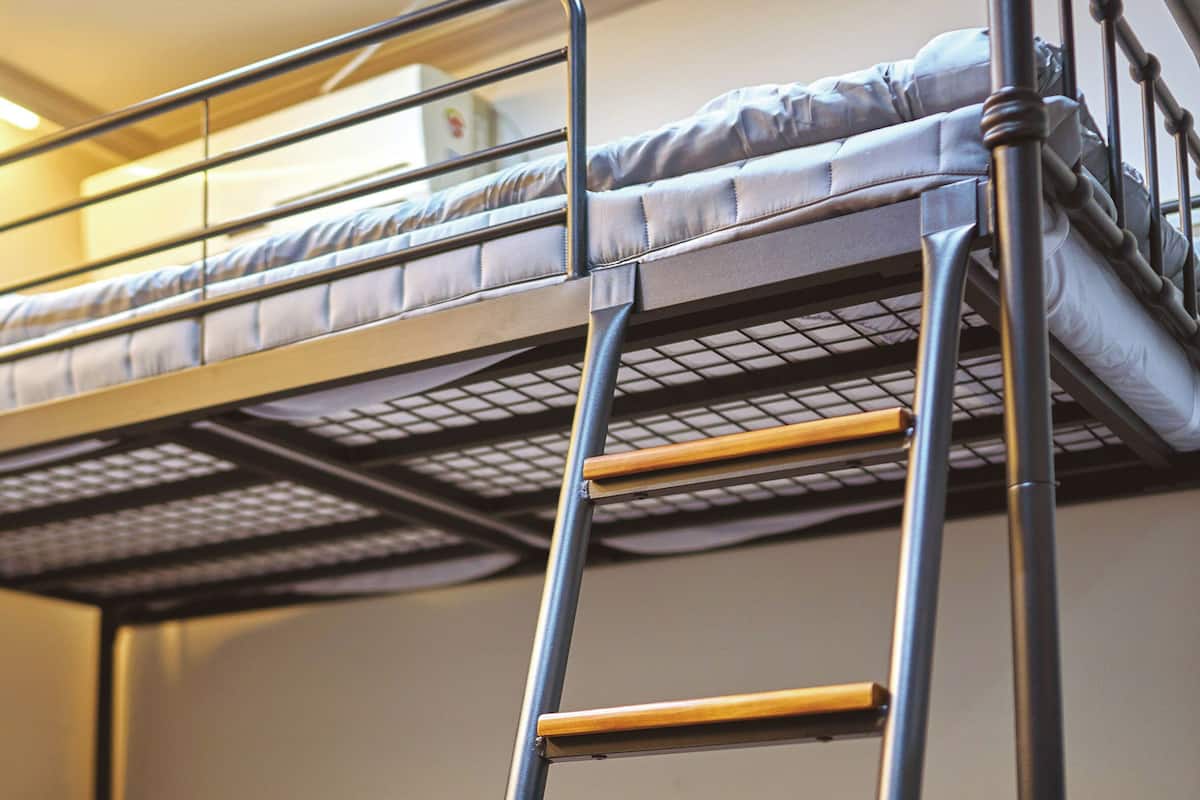 A bunk bed with a ladder, wooden headboard, and a mattress with a striped cover.