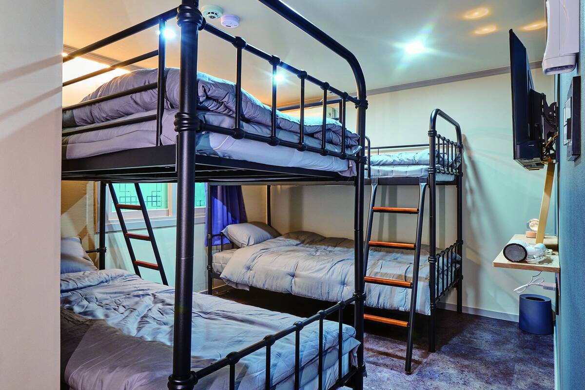 A bunk bed room with a ladder, a desk with a chair, and a television on the wall.