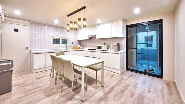 Une cuisine moderne avec des meubles blancs, une table à manger avec des chaises et des luminaires suspendus.