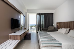 A modern hotel room with a large bed, a desk with a flat-screen TV, a seating area with a chair, and a balcony with a view.