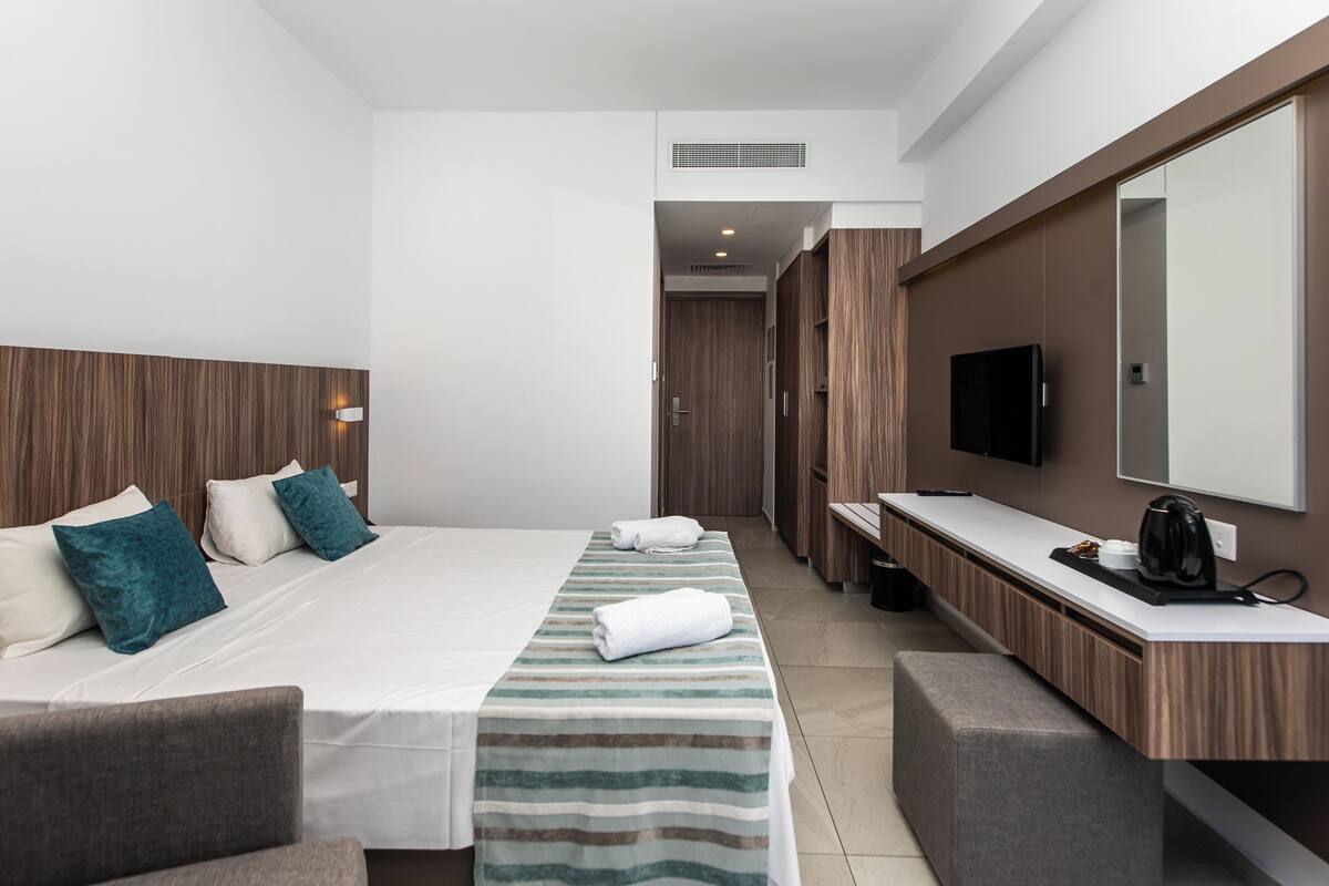 A modern hotel room with a large bed, a bedside table, a mirror, and a TV.