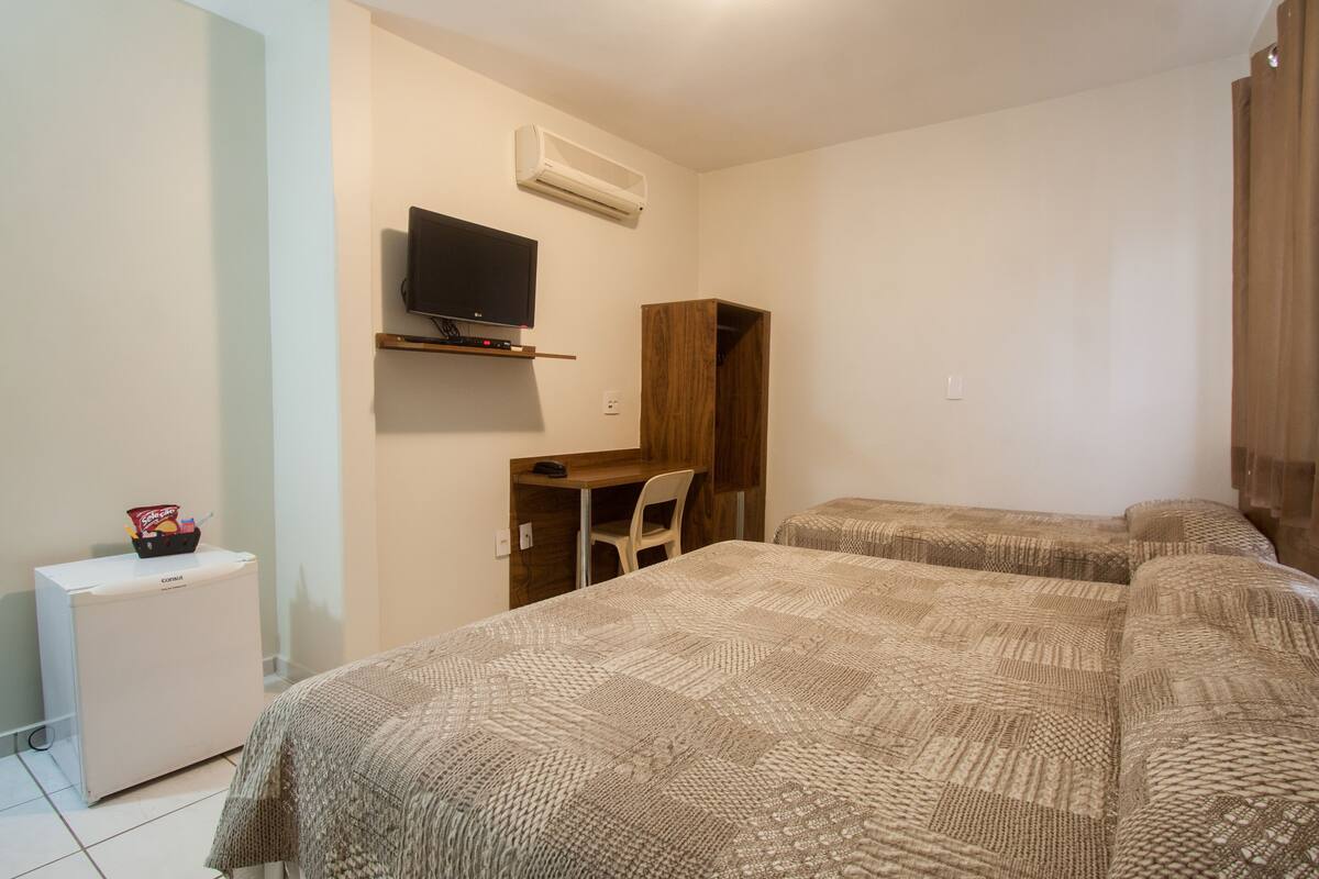 A bedroom with two beds, a desk, a chair, a TV, and a small fridge.
