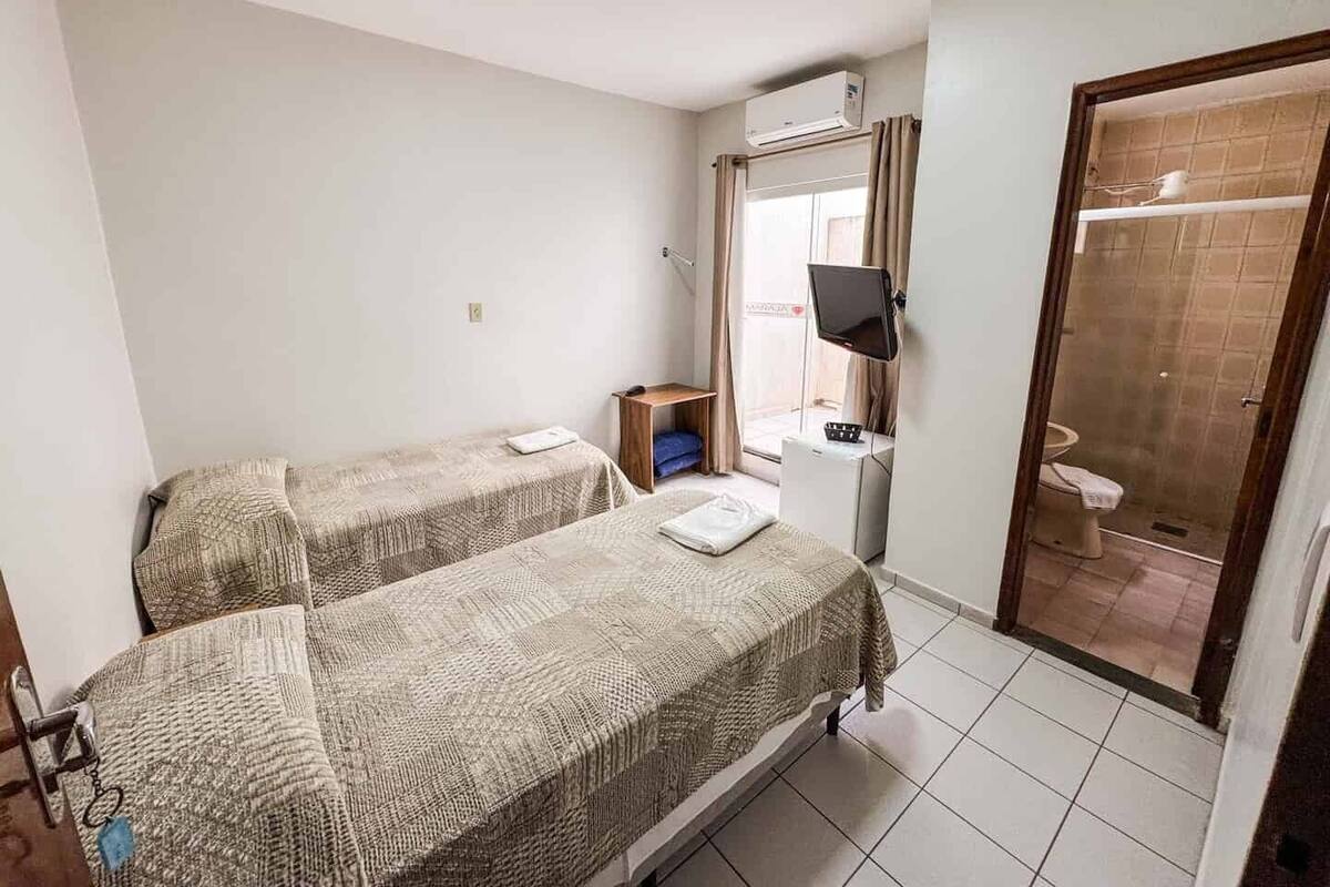A small hotel room with two beds, a desk, a chair, a TV, and a bathroom visible through an open door.