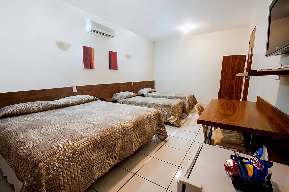 A hotel room with two beds, a wooden table, a TV, and a wall-mounted air conditioner.