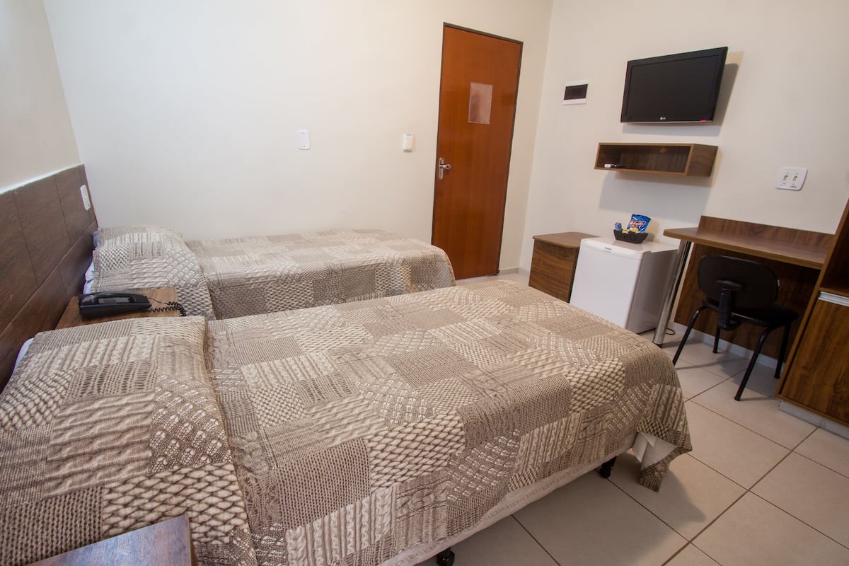 A hotel room with two beds, a desk, a television, and a small refrigerator.