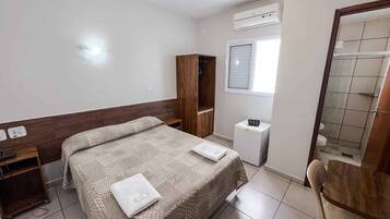 A bedroom with a bed, a wardrobe, a small desk, and a shower area.