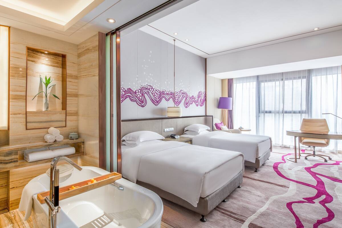 A hotel room with two beds, a bathtub, a desk, and a chair.