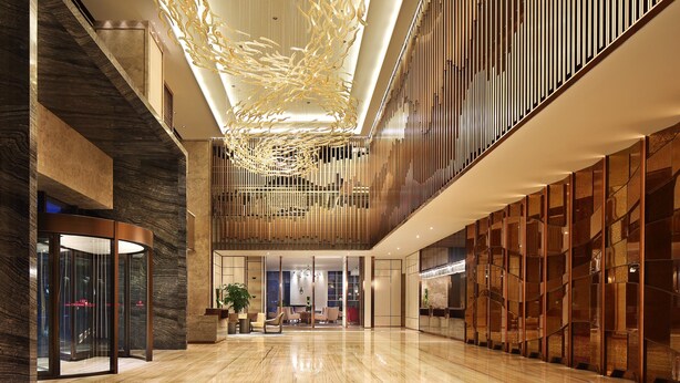 Un hall d’entrée spacieux avec un plafond haut, un lustre moderne et un comptoir d’accueil.