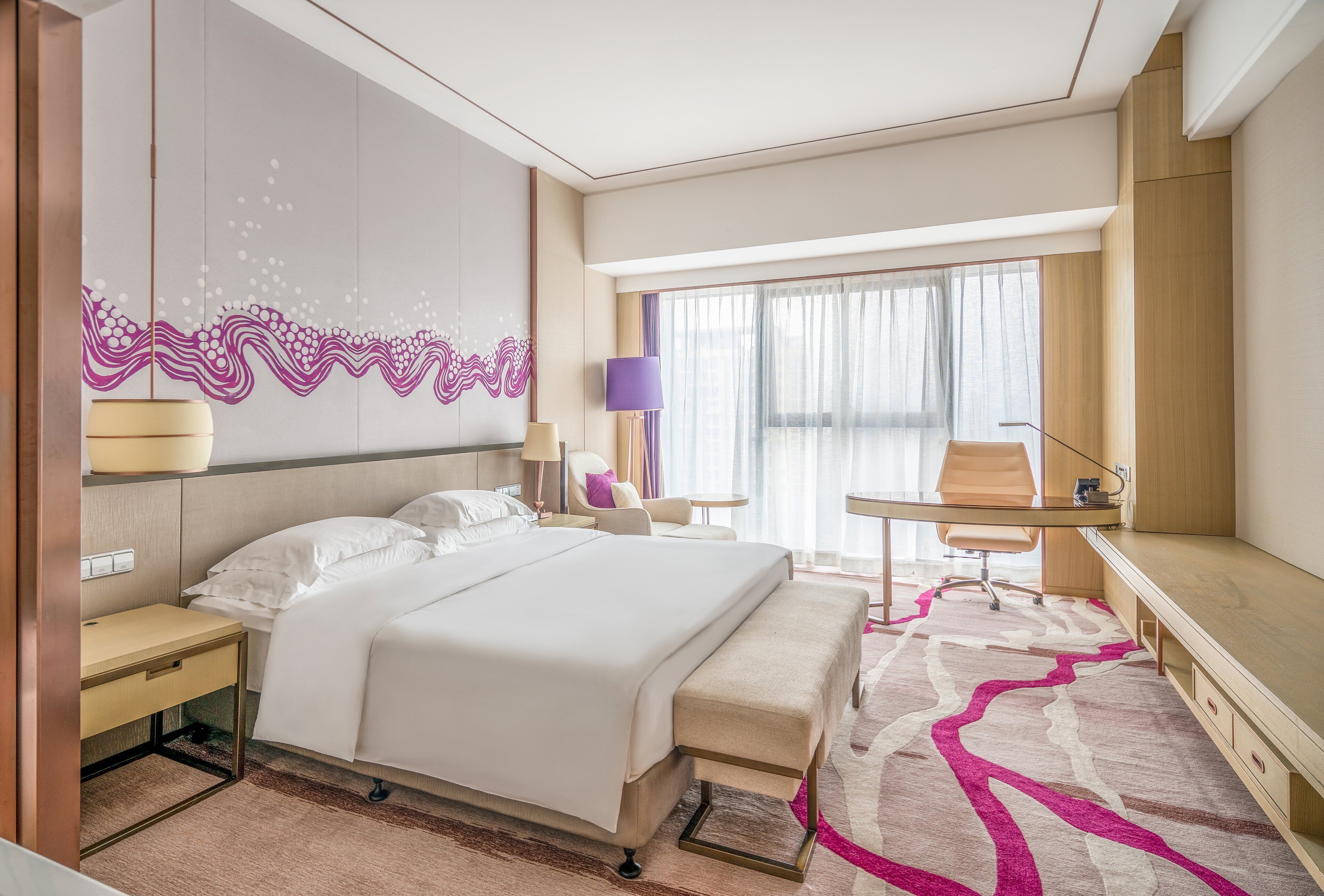 A modern hotel room with a large bed, a desk, a chair, and a view of the city through large windows.