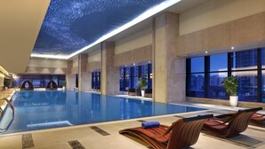 Une vaste piscine intérieure offrant une vue dégagée sur le paysage urbain grâce à de grandes fenêtres.