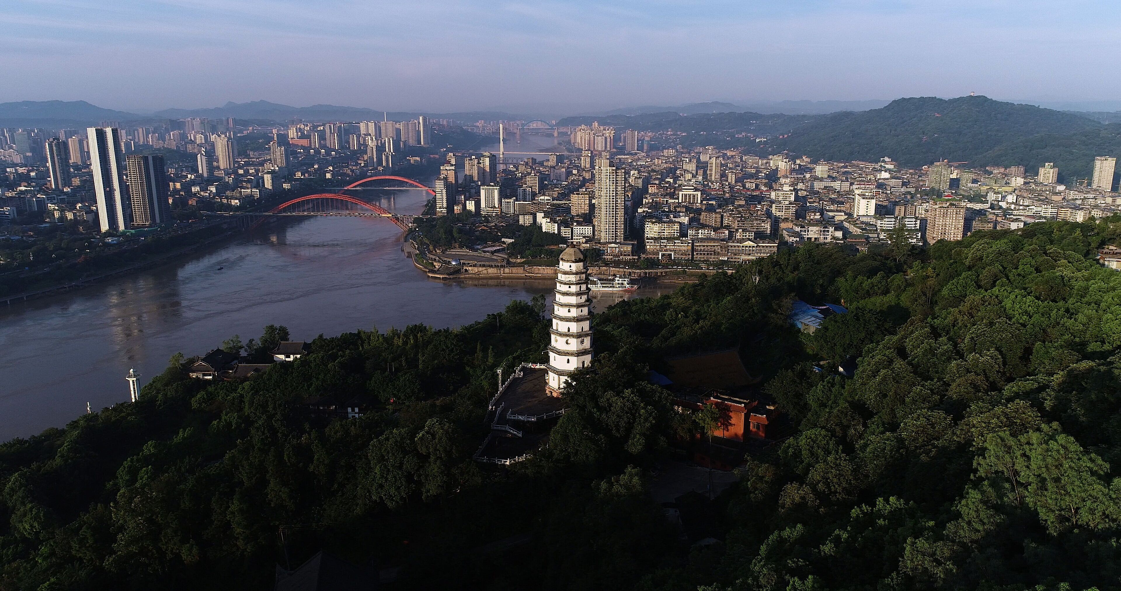 Une vue urbaine avec une pagode imposante, un pont rouge et une rivière.