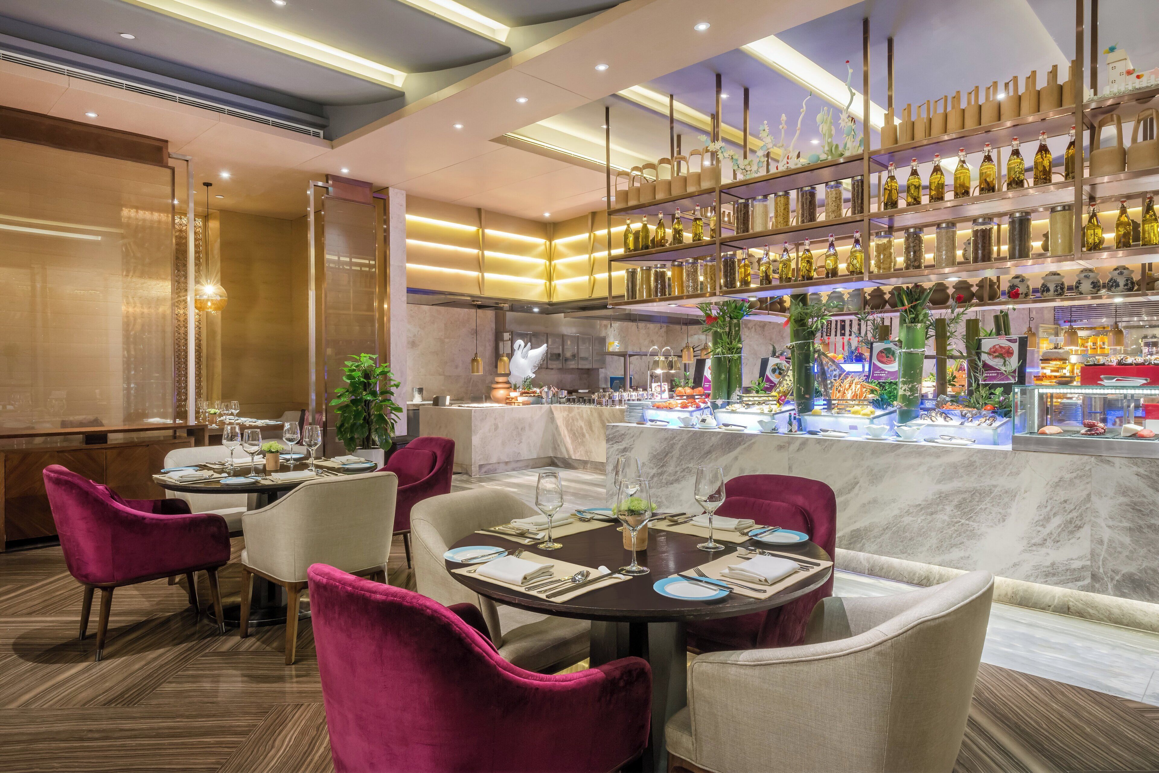 A restaurant interior with round tables, plush chairs, and a bar area with shelves of bottles.