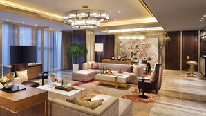 Un salon spacieux comprenant un grand canapé, une table basse et un téléviseur. On y trouve également un coin repas avec une table et des chaises, ainsi qu’un élément décoratif mural.