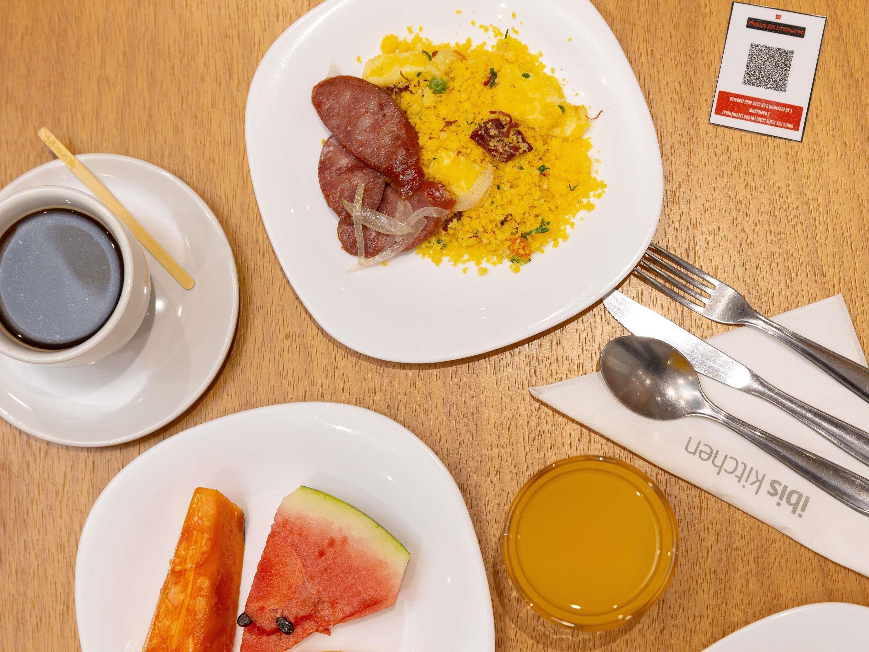 Un plato con arroz, salchicha y verduras, una taza de café y un vaso de jugo sobre una mesa de madera.