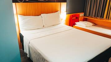A hotel room with a large bed, a smaller bed, a red chair, and a nightstand with a lamp.