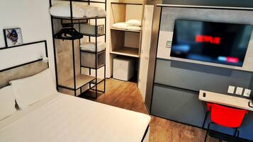Habitación de hotel compacta con cama, televisor, escritorio pequeño y armario con estantes.