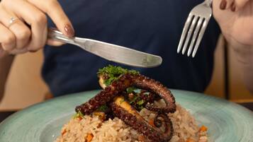 A person holding a fork and knife, about to eat a meal with octopus tentacles on top of rice.