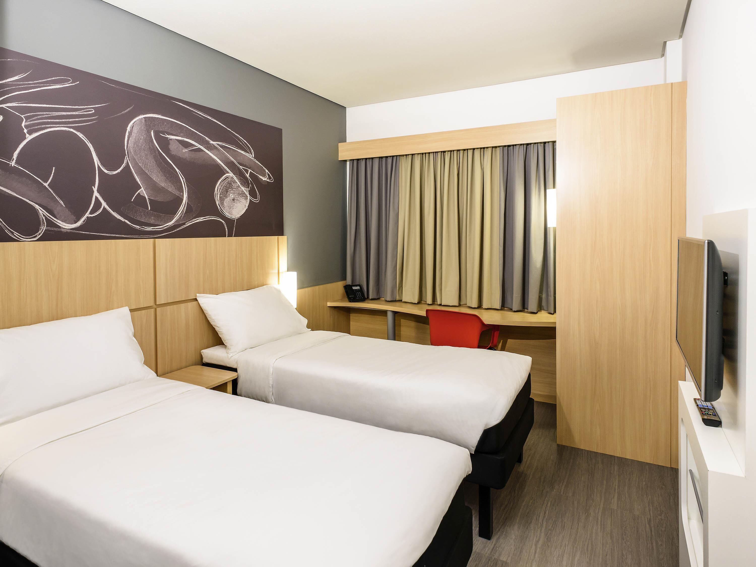 A hotel room with two beds, a desk, a chair, a television, and a wall art piece.