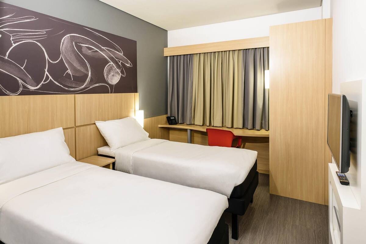 A hotel room with two beds, a desk, a chair, a television, and a wall art piece.