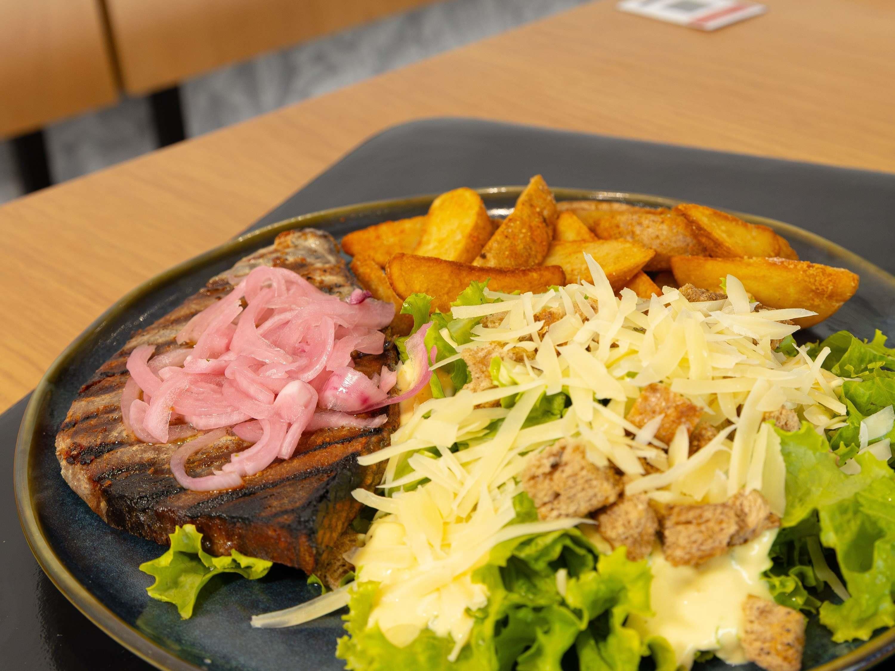 Un plato con carne a la parrilla, papas fritas, queso rallado y una ensalada.
