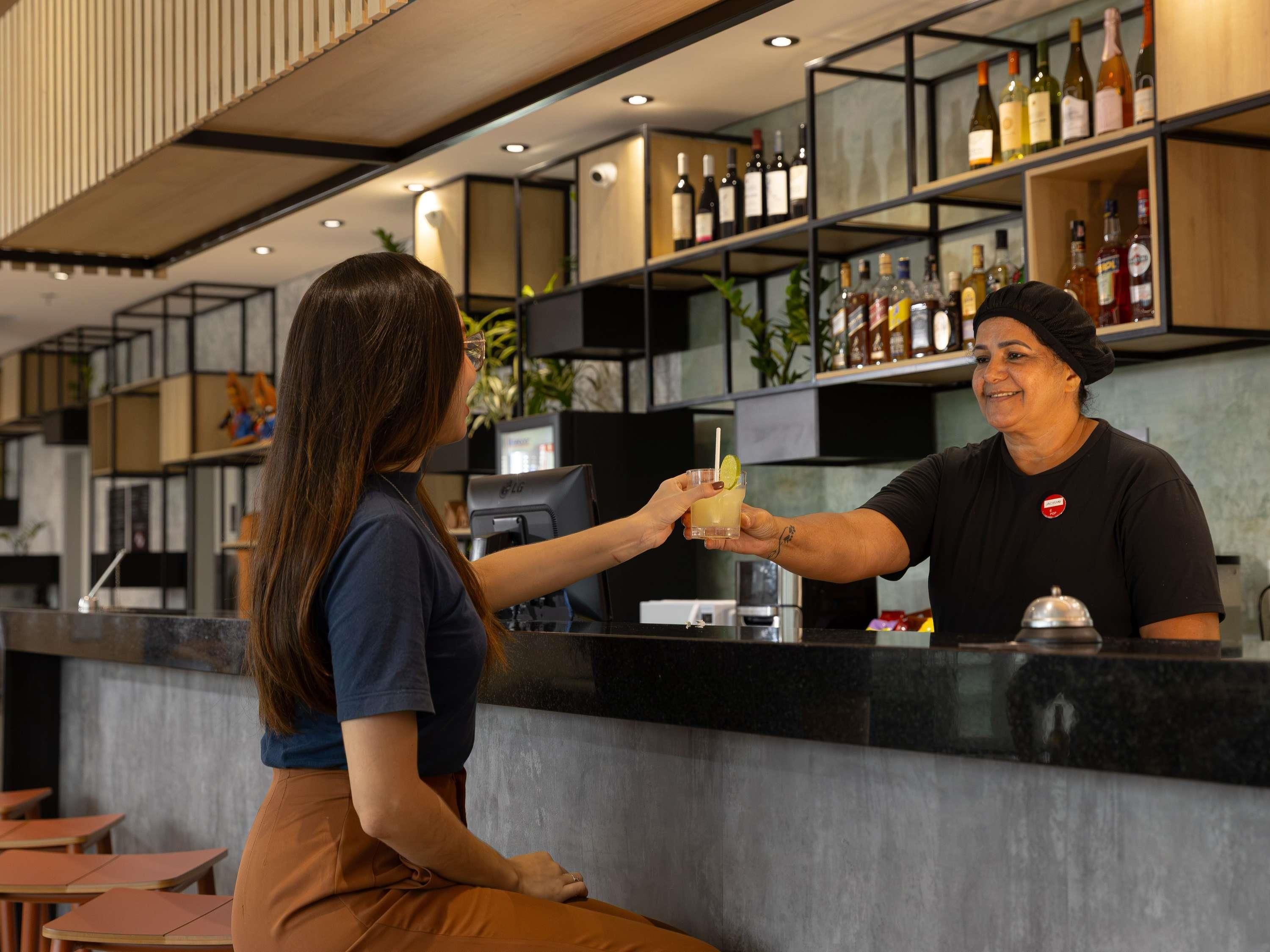 Zona de bar con mostrador, estanterías llenas de botellas y un espacio de estar con mesas.