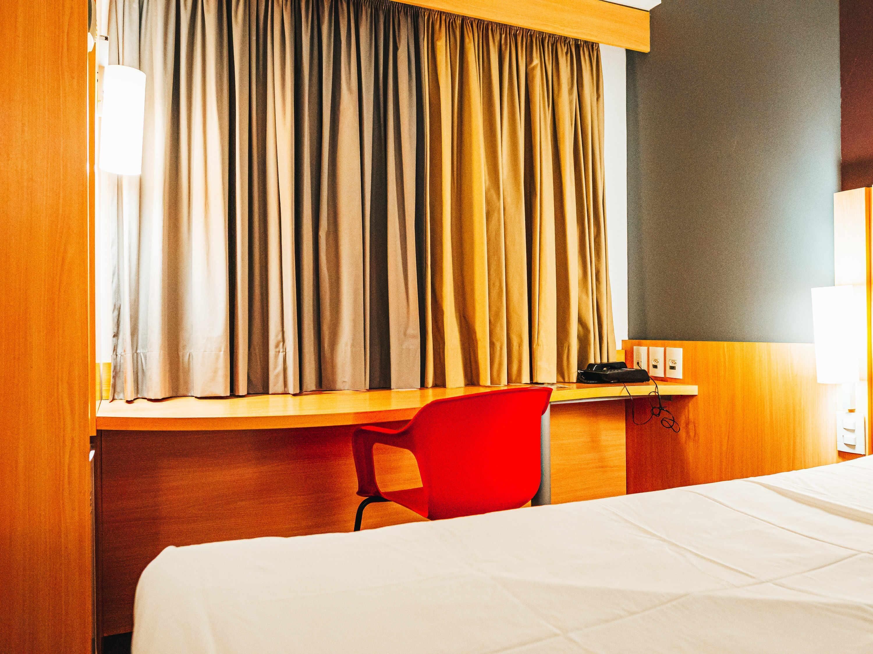 A hotel room with a bed, a desk, a chair, and a window with curtains.