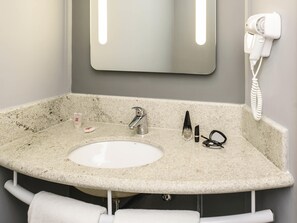 Un baño con lavamanos de granito, un espejo, un secador de pelo y un perchero para toallas.