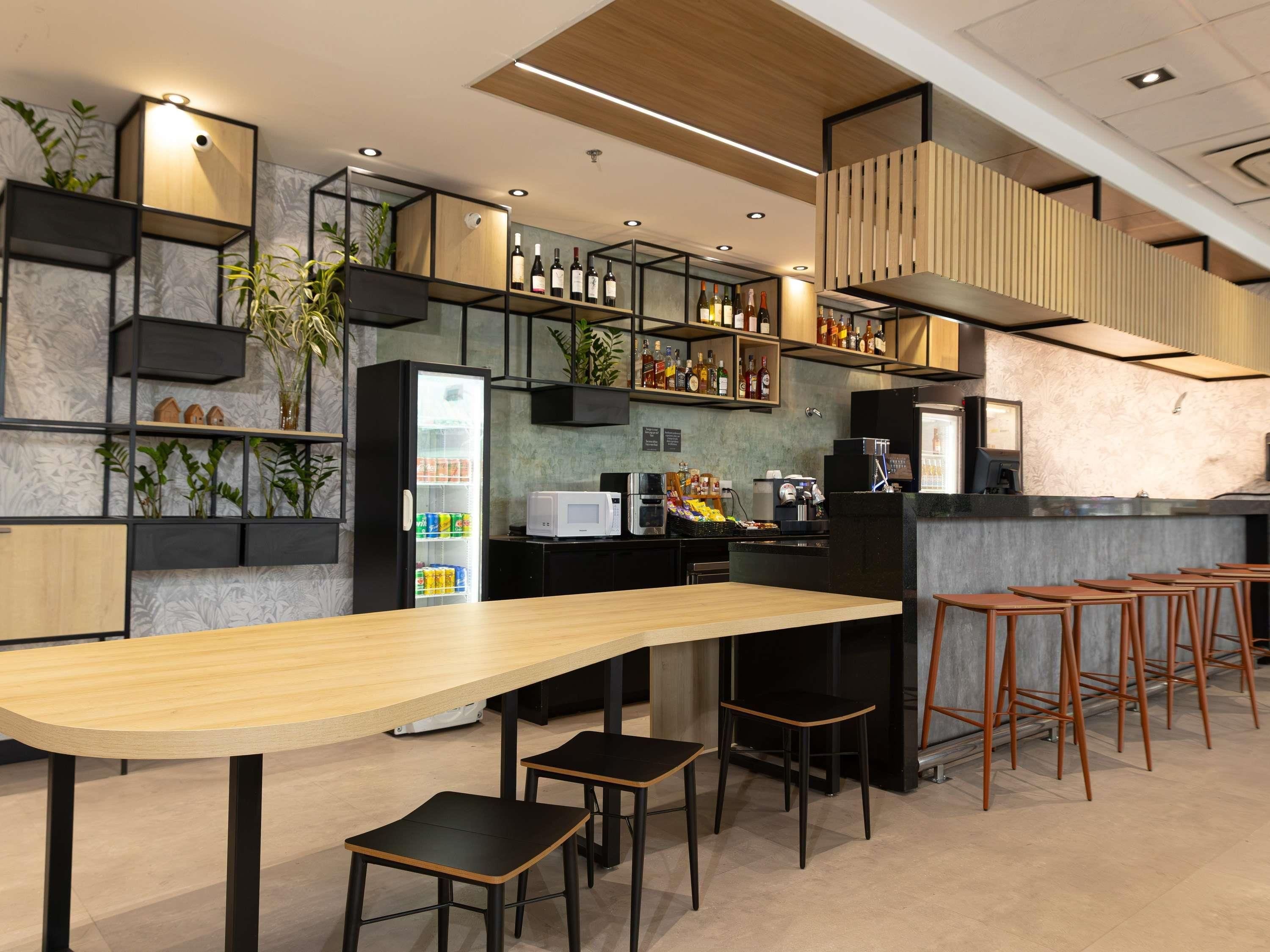 Uma área de bar moderna com um balcão comprido, banquetas e prateleiras cheias de garrafas.
