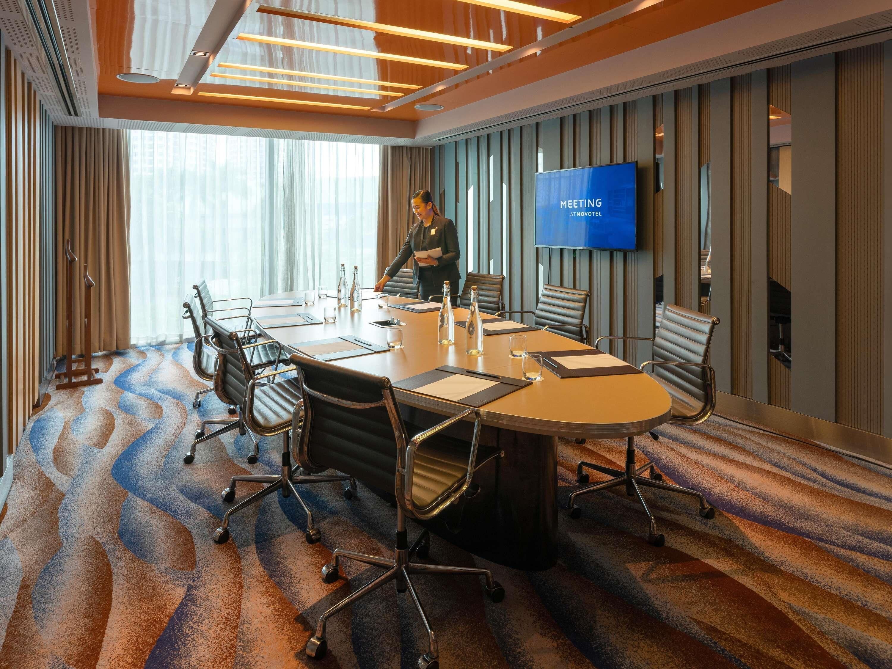 A meeting room with a large table, chairs, a TV screen, and a patterned carpet.