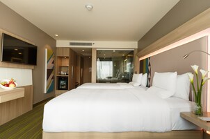 Ein modernes Hotelzimmer mit einem großen Bett, einem an der Wand befestigten Fernseher, einem Nachttisch mit Blumen und Blick ins Badezimmer.