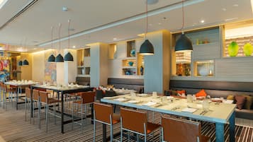 A modern restaurant with multiple dining tables and chairs, pendant lighting, and decorative shelves.