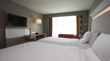 A hotel room with two beds, a flat-screen TV, a desk, and a window with curtains.
