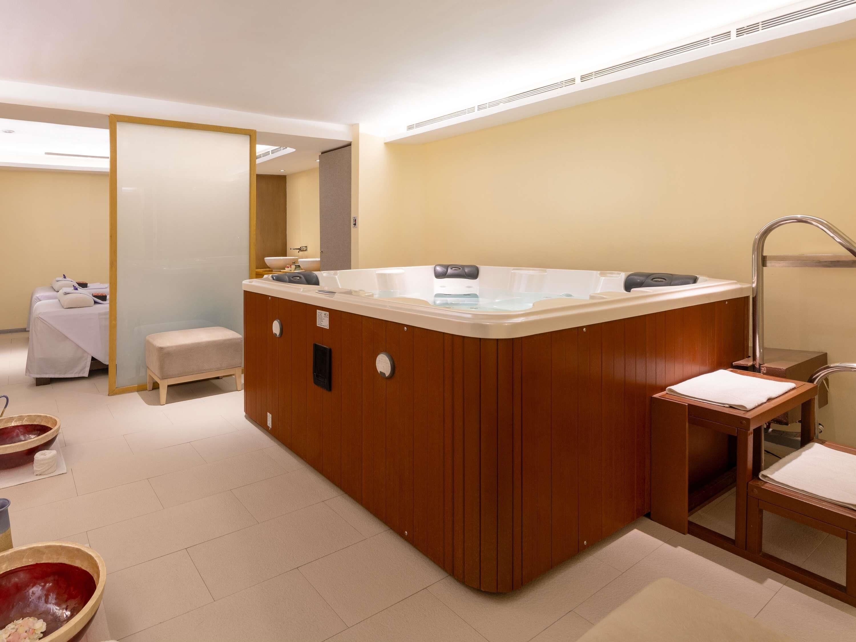Ein modernes Badezimmer mit einer Holzbadewanne, einer Sitzbank und einem Waschbecken mit Spiegel.