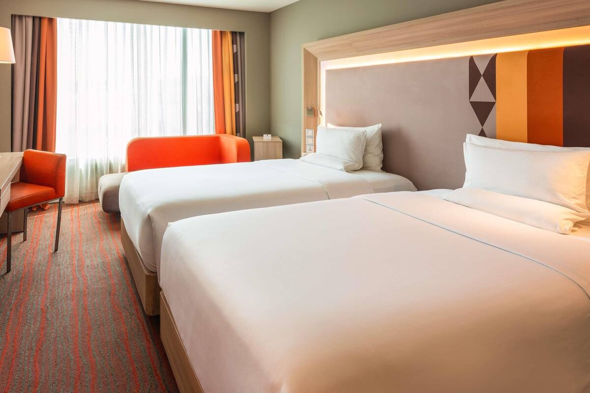 Une chambre d’hôtel avec deux lits, un bureau, une chaise et une vue sur l’extérieur.