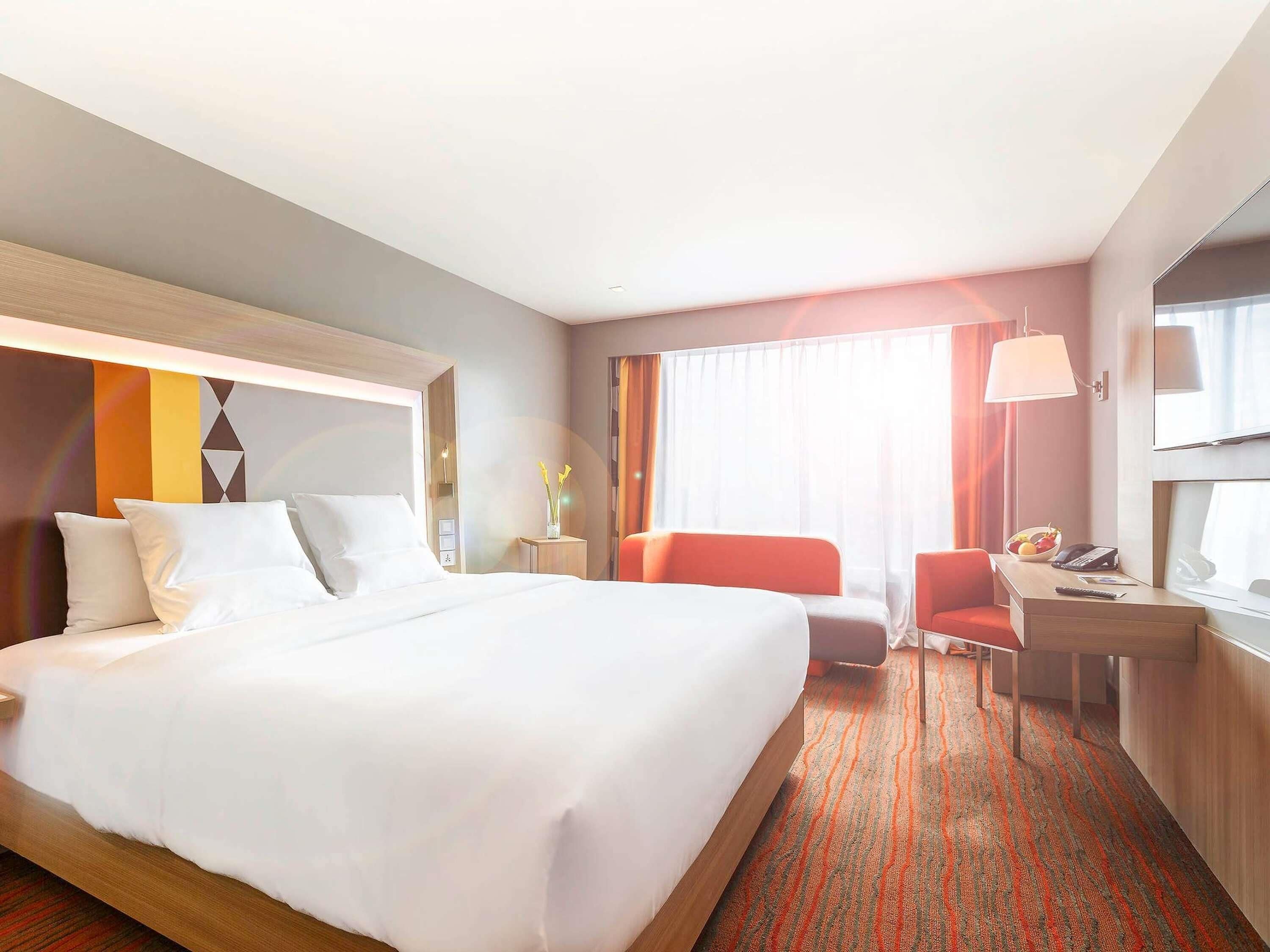 A hotel room with a large bed, a desk with a chair, a television, and a window with curtains.