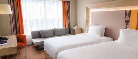A hotel room with two beds, a desk, a chair, and a sofa.