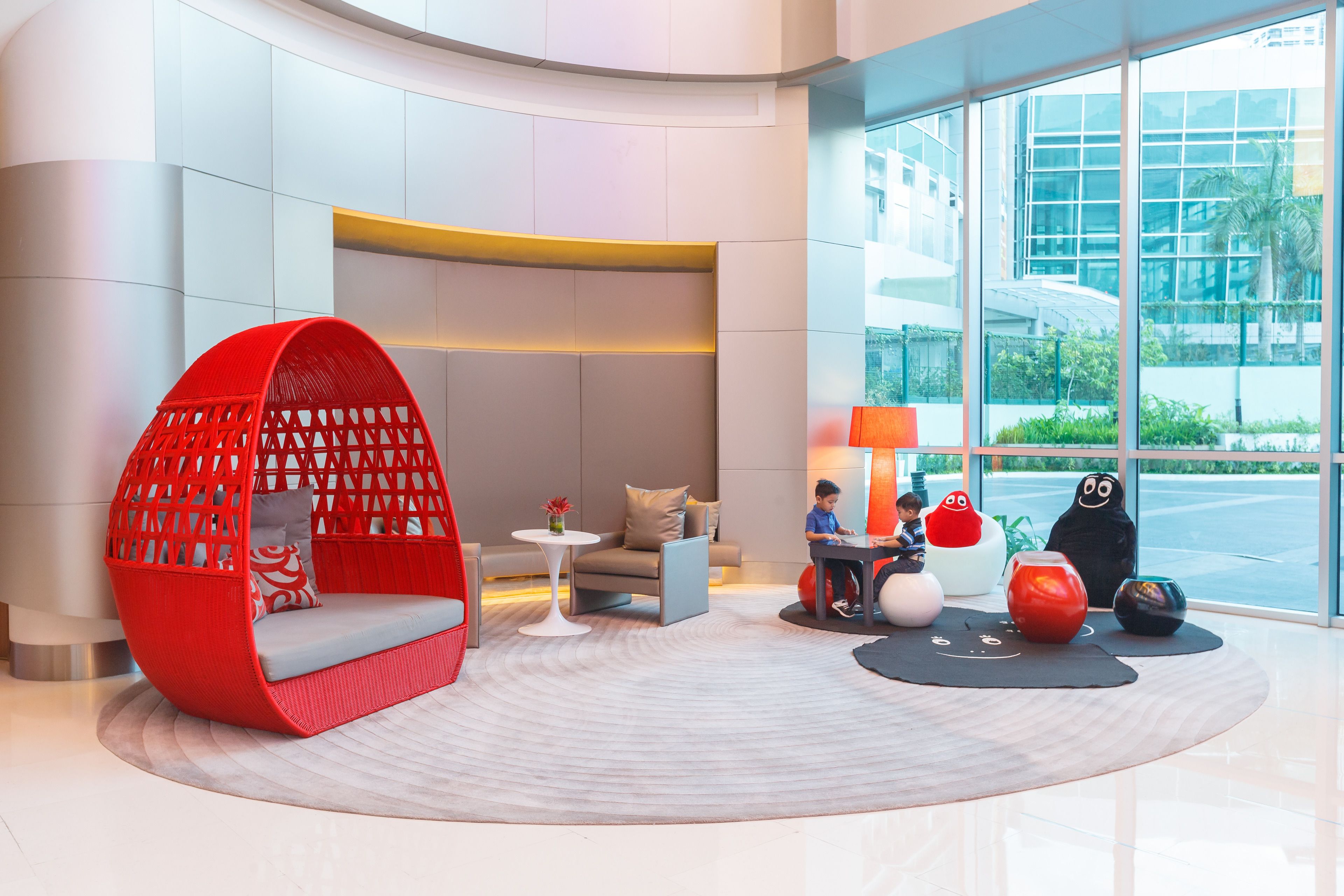 Un hall d’entrée moderne avec un fauteuil suspendu rouge, un canapé, une petite table et des objets décoratifs.