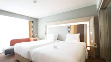 A hotel room with two beds, a small table with a lamp, and a window with curtains.