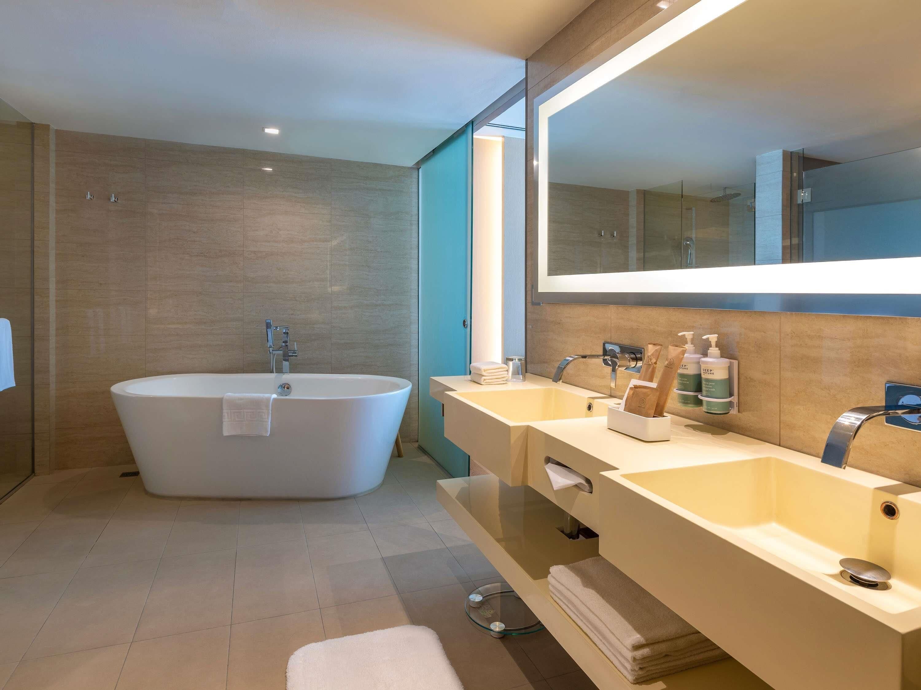 A modern bathroom with a freestanding bathtub, two sinks, and a large mirror.