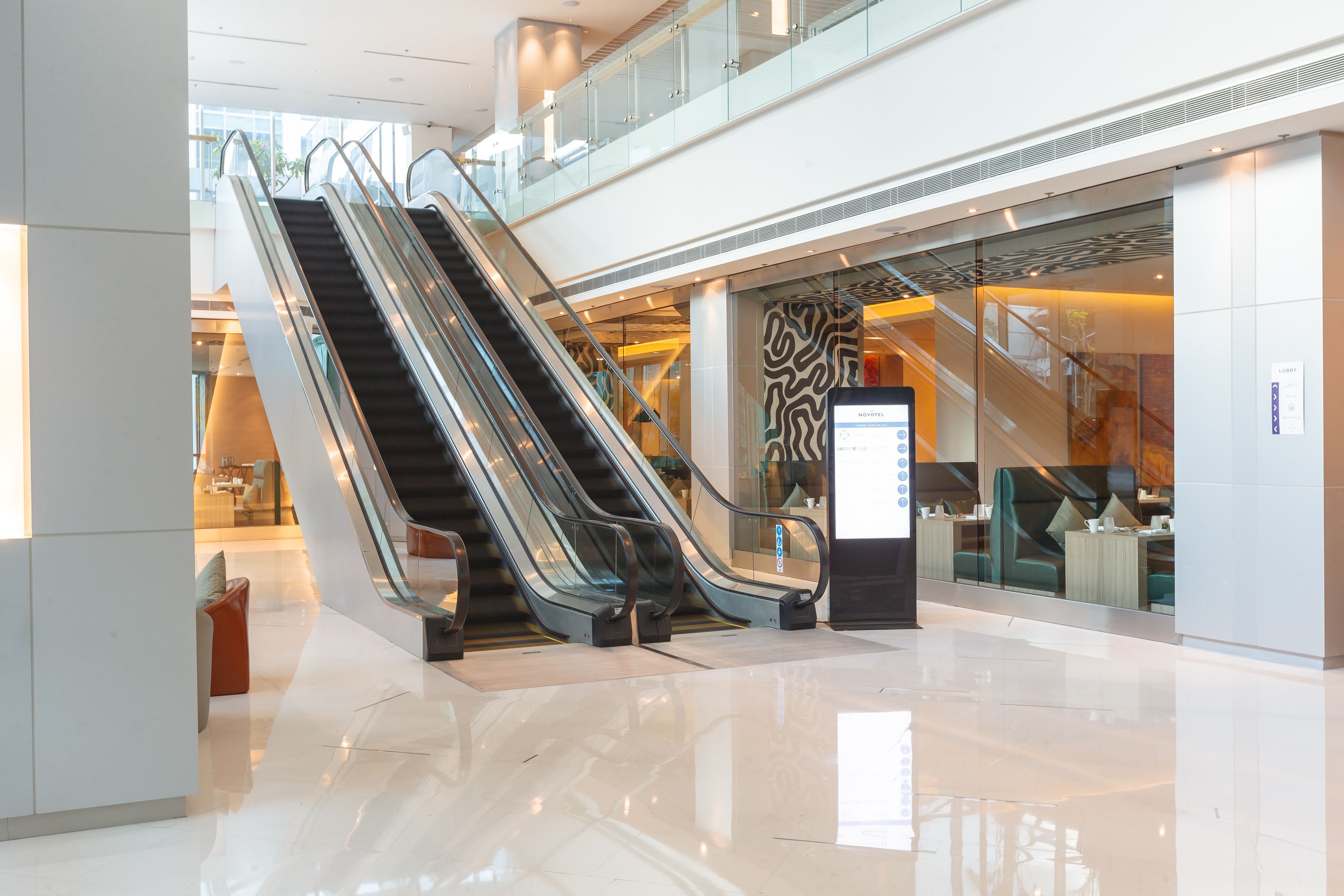 A modern shopping mall with escalators, a glass storefront, and a clean, polished floor.