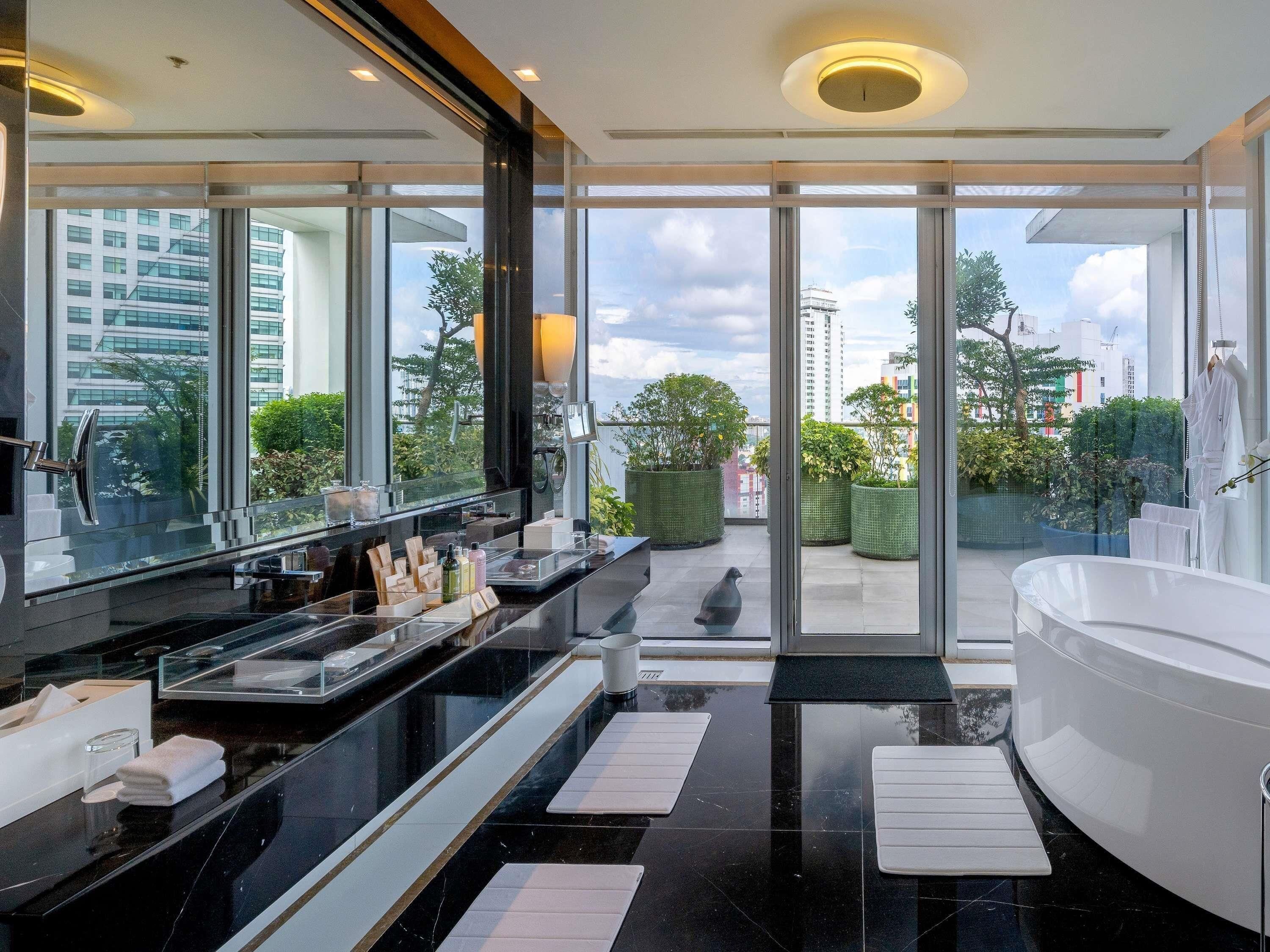 A modern bathroom with a large bathtub, a vanity with a mirror, and a view of the city through large windows.